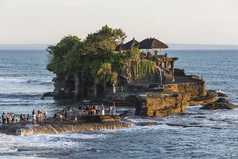 The sea temple of Tanah Lot on its rock, with visitors on the reef below at low tide