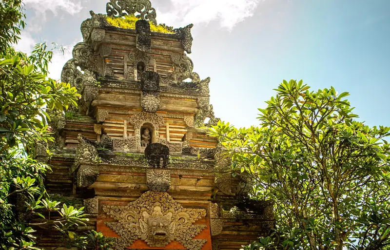 A carved stone gateway at Ubud Palace, framed by frangipani trees