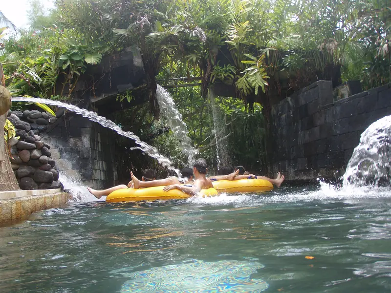Children floating on rings down the lazy river at Waterbom Bali, among tropical planting